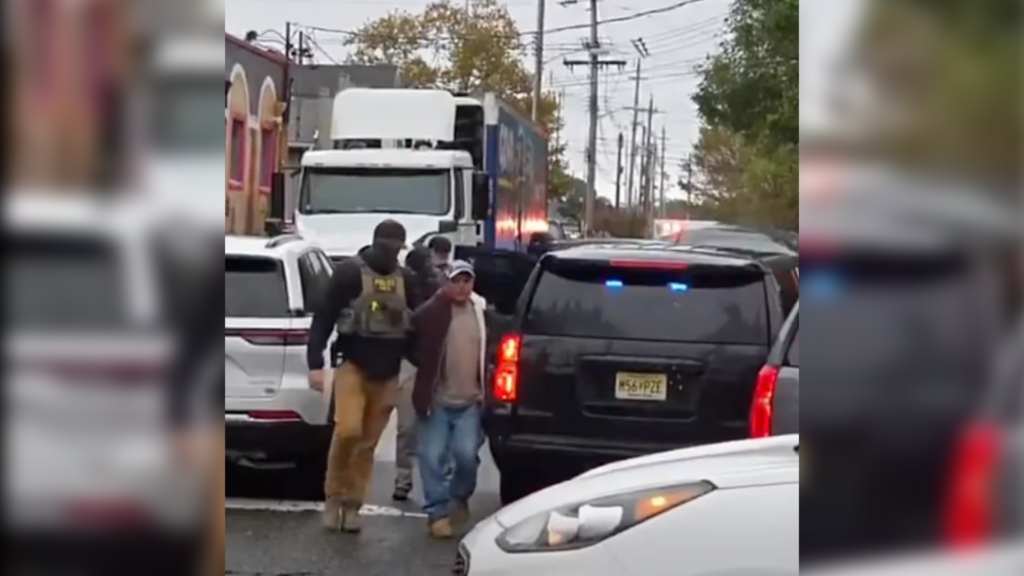 Federal immigration agents escort a man past vehicles on a street in Red Bank, New Jersey.